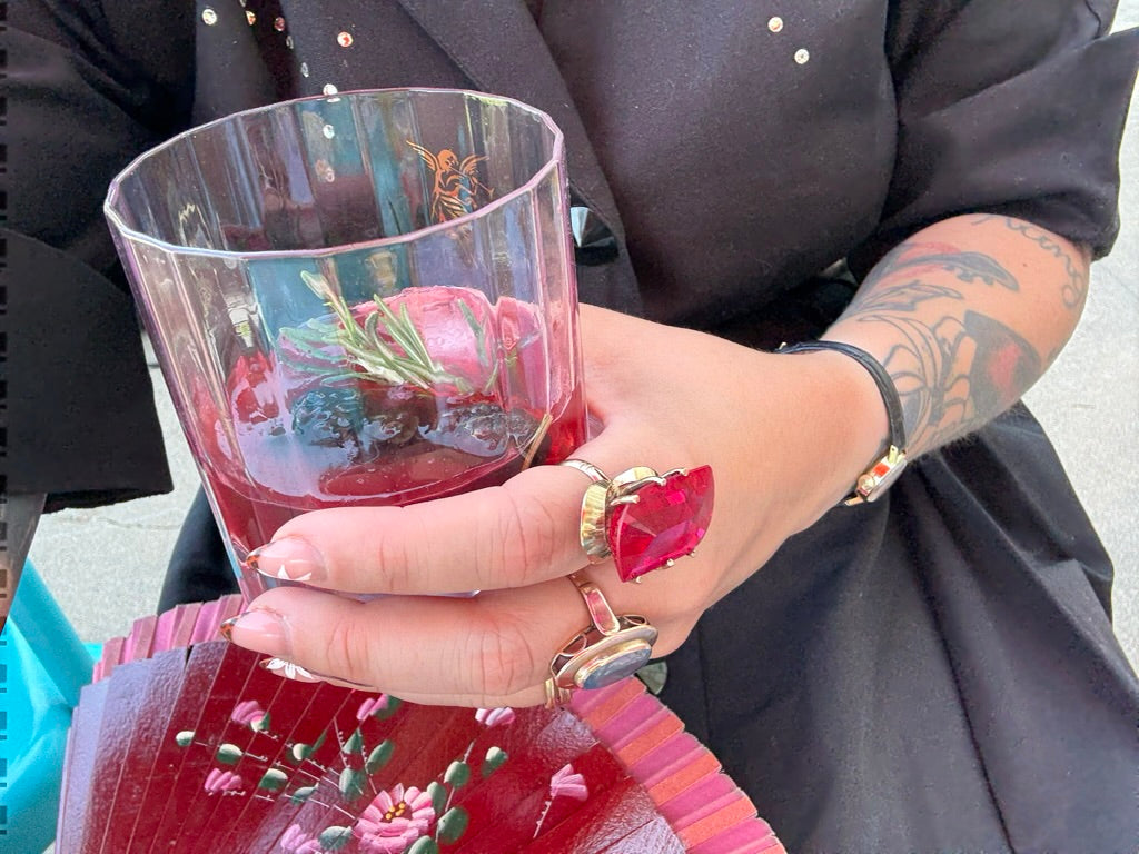 Person holding a glass with floral design, wearing a ring and bracelet.